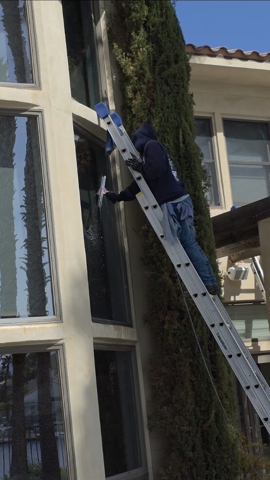 Technician on a ladder cleaning tall exterior windows in Las Vegas